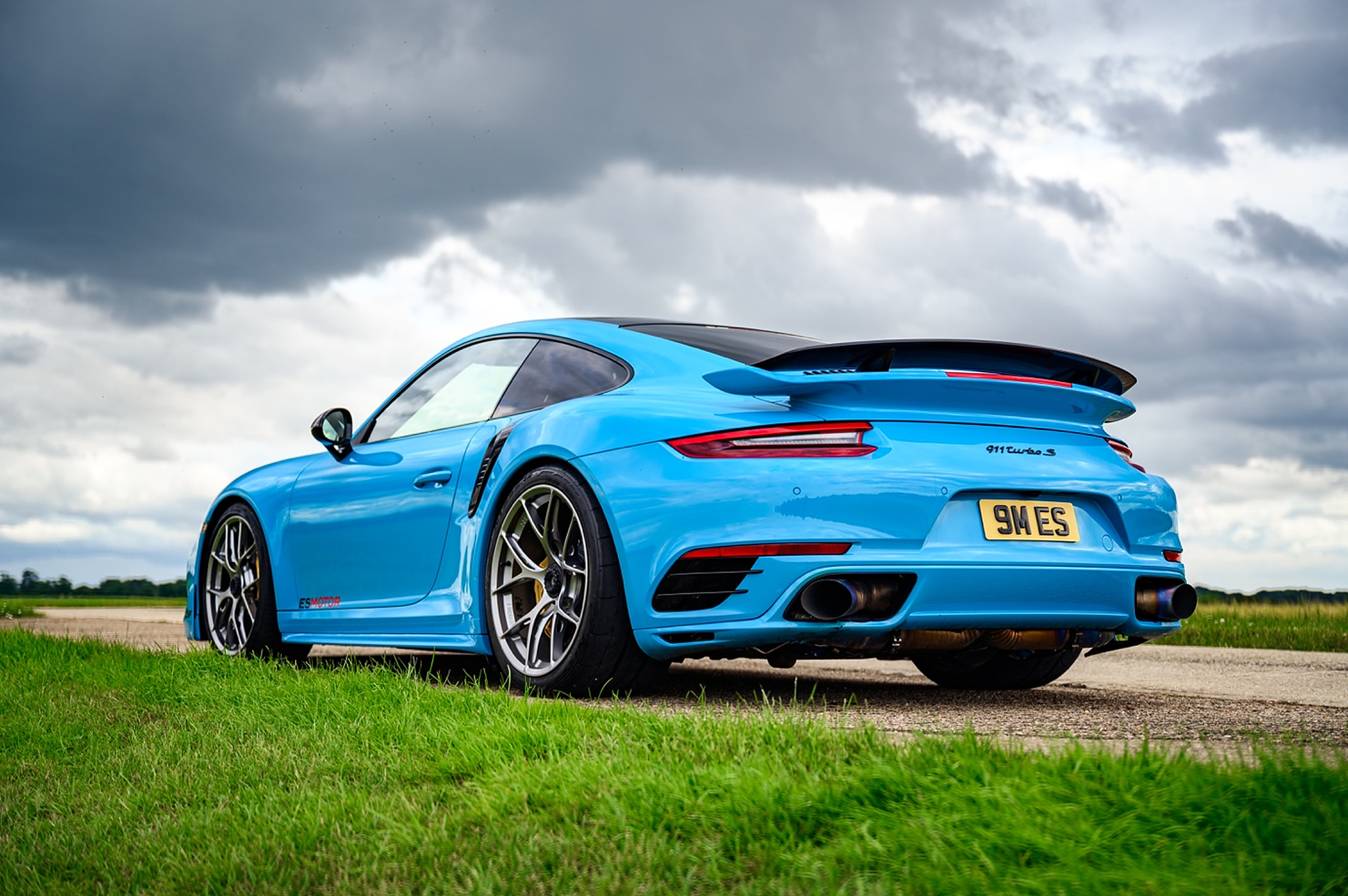 Blue Porsche 911 Turbo S on grass under a cloudy sky